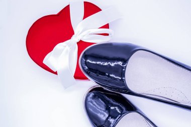 Kadınların siyah deri ayakkabıları. Bir tanesi beyaz kurdeleli, kalp şeklinde kırmızı bir ipek kutuya basmış..