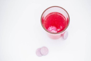 Pembe su dolu bir bardakta, çözünebilir, hazır ya da erimiş pembe tablet baloncukları. Yakınlarda benzer haplar var: C vitamini, beslenme takviyeleri, ağrı kesiciler. Beyaz arkaplan, alanı kopyala.