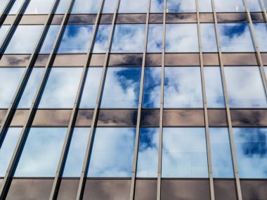 Bulutlu mavi gökyüzü modern ofis binasının aynı pencerelerinin camına yansıyor..