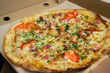 Jambonlu, peynirli, domatesli, otlu ve pastırmalı yuvarlak pizza. Fast food teslimatı.