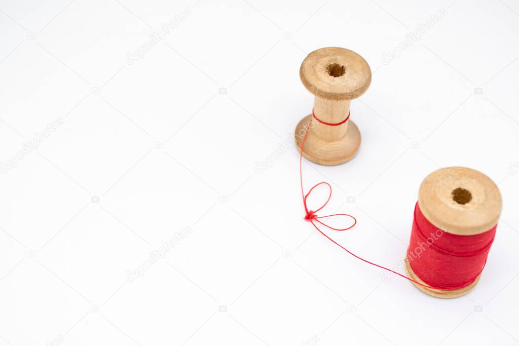 Two wooden spools of thread. One is full, the other almost empty, connected by a single thread. Togetherness as a concept, no people, without people.