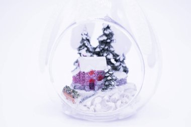 Karlı bir ormandaki küçük evin yakınında şeffaf Noel balosunun içinde, beyaz arka plan, fotokopi alanı. Sıcak kış tatili konsepti.