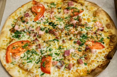 Jambonlu, peynirli, domatesli, otlu ve pastırmalı yuvarlak pizza. Fast food teslimatı.
