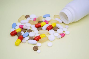 Sarı arka planda beyaz bir şişeden çok renkli haplar düşüyor..