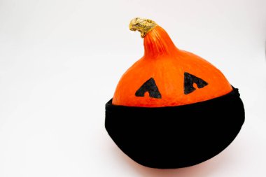 Cadılar Bayramı ve covid-19: beyaz arka planda siyah maskeli parlak turuncu bir balkabağı. Uzayı kopyala Boo! .