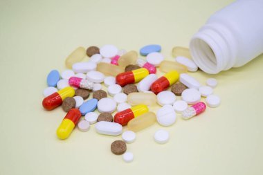 Sarı arka planda beyaz bir şişeden çok renkli haplar düşüyor..