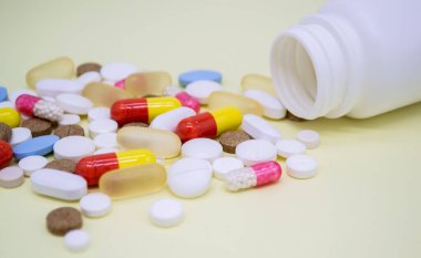 Sarı arka planda beyaz bir şişeden çok renkli haplar düşüyor..