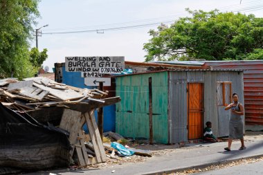 Cape Town, Güney Afrika - 4 Aralık 2015: Kaynak dükkanı ve kıvrımlı demir çatılı yeşil ev, kasaba. Genç bir kadın ve bir çocuk sokakta oturuyor..