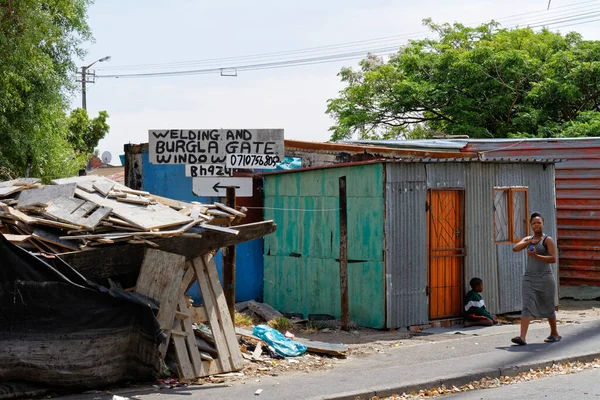 Cape Town, Güney Afrika - 4 Aralık 2015: Kaynak dükkanı ve kıvrımlı demir çatılı yeşil ev, kasaba. Genç bir kadın ve bir çocuk sokakta oturuyor..