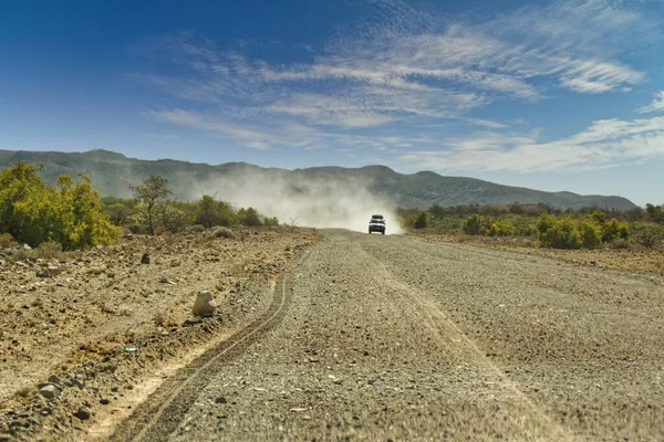 Pickup truck jede rychle na dlouhé rovné pouštní silnici. Teplý slunečný den s modrou oblohou. Afrika-Namibie — Stock fotografie