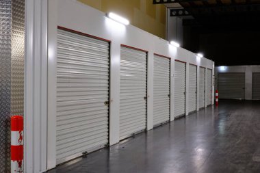 Bir depolama tesisinde beyaz kapılar var. Kiralık Depo Birimleri ve kırmızı beyaz güvenlik direği. Hollanda