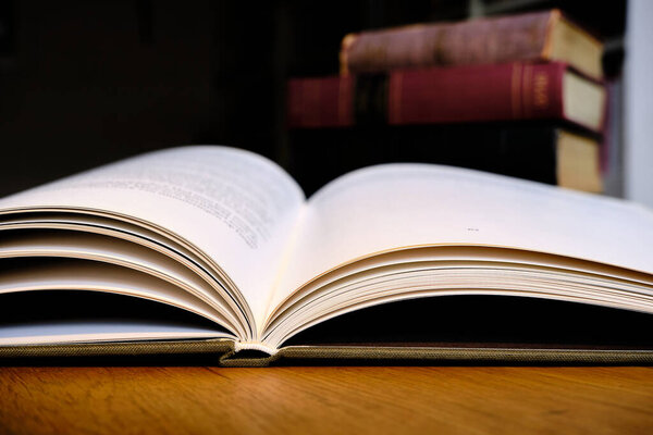 Закрытие открытой учебной книги на деревянном столе в библиотеке. Старые книги и книжная полка фон. Концепция образования. Селективный фокус
