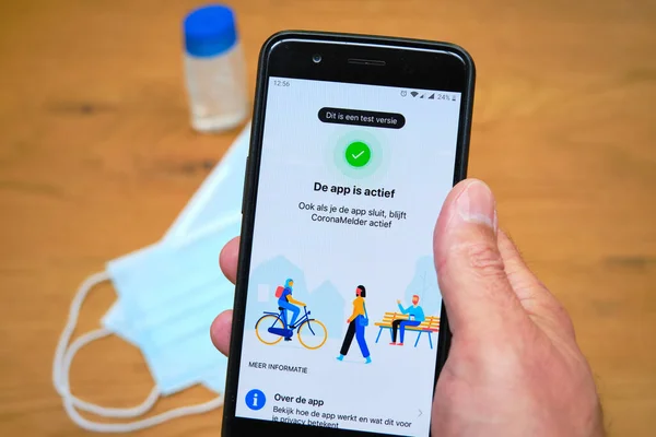 Bennekom, Hollanda, Juli, 7.2020: Hollandalı Corona izleme uygulaması olan akıllı telefon: Coronamelder. Yüz maskesi ve dezenfektan. Hollandaca metin: Bu bir test sürümü. Uygulama kapatıldığında bile etkin.