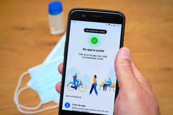 Bennekom,Netherlands,Juli,7,2020:Smartphone with Dutch Corona tracking app named:Coronamelder. Face mask and disinfectant. Dutch text:This is a test version.App is active even when app closes. — Stock Photo, Image