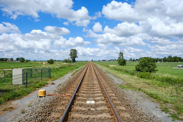 Single track railway for diesel train through typical Dutch grassland area, Friesland district. Sunny day with blue sky and white clouds, the Netherlands.