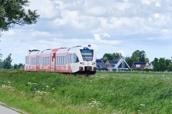 Boazum, Friesland, Hollanda, 21 Temmuz 2020: Hollanda 'nın tipik çayır bölgesi üzerinden Stavoren' e giden Arriva dizel yolcu treni. Güneşli bir gün, mavi gökyüzü ve beyaz bulutlar, Hollanda.