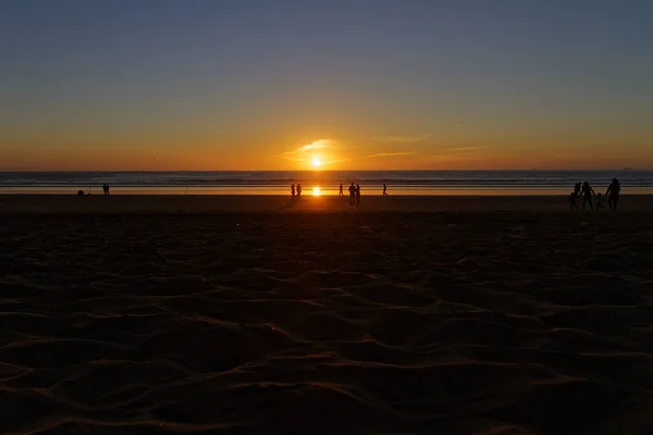 Normale alledaagse donkere zonsondergang scène met silhouetten van mensen lopen op een strand en kijken naar de zonsondergang. Romantische avond met zonsondergang op Afrikaans strand. Marokko, Agadir — Stockfoto