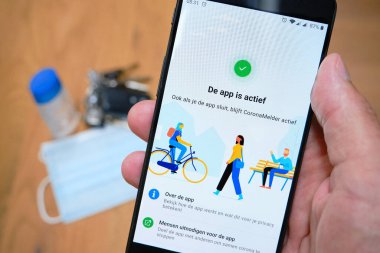 Bennekom, Hollanda, Aug, 20,2020: Hollanda Corona izleme uygulamalı akıllı telefon: Coronamelder. Yüz maskesi, dezenfektan ve anahtarlar. Flemenkçe metin: Uygulama uygulama kapatıldığında bile etkin, uygulama insanları davet ediyor