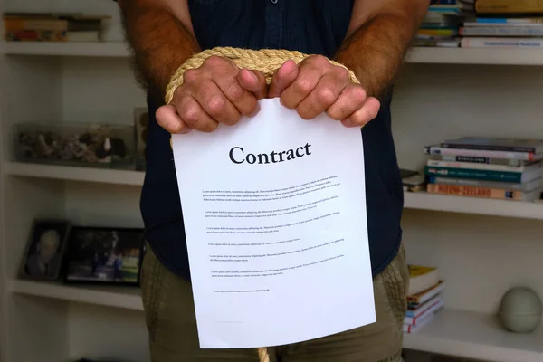 Tied hands holding contract paper in front of bookcase. Bound man hands with paper contract, breach of contract. Unfair agreement. Lorum Ipsum text