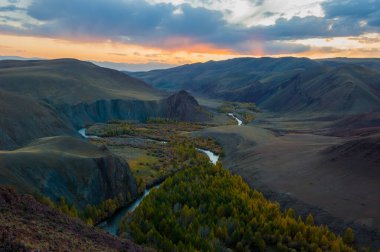 Gün batımı, dağların ve sonbahar ağaçlarının arka planında akan nehir, Altai.