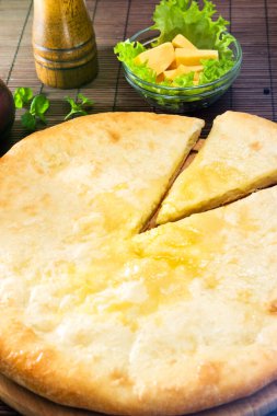 Tahta tezgahta peynirli Osetya turtası ve içinde malzemeler olan kahverengi bir Mat. Bir parçası kesilmiş..