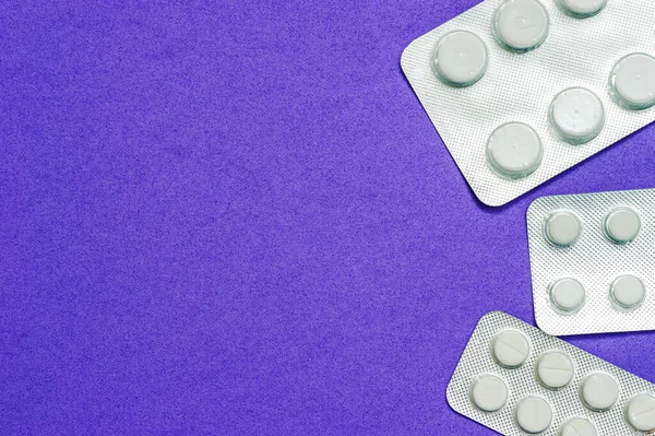 Tres paquetes brillantes de pastillas blancas sobre un fondo azul. Enfermedades, productos farmacéuticos . — Foto de Stock