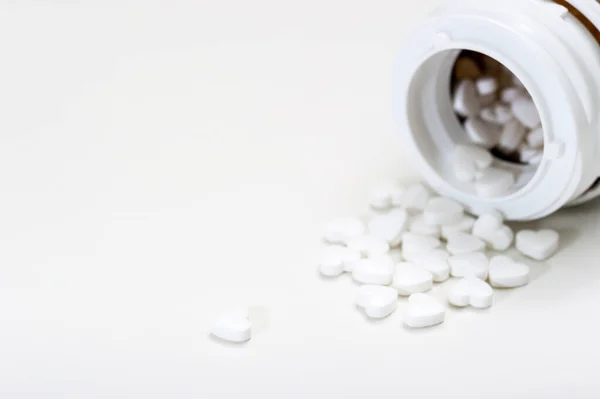 Píldoras en forma de corazón sobre un fondo blanco se vierten fuera del frasco, productos farmacéuticos . — Foto de Stock