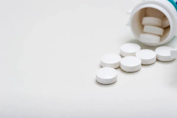 Las tabletas se vierten fuera del frasco sobre un fondo blanco. Vitaminas, medicamentos, vista frontal . — Foto de Stock