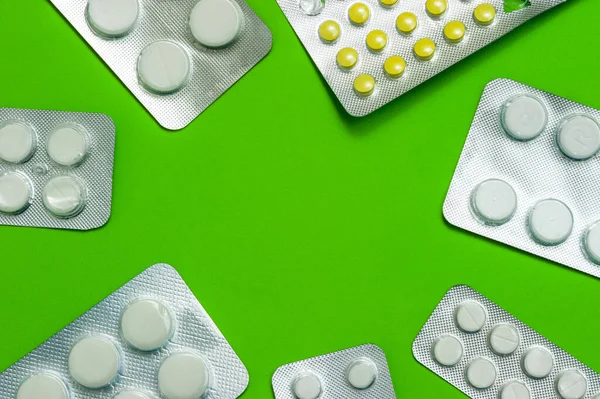 Un grupo de paquetes brillantes de comprimidos blancos y amarillos sobre un fondo verde se encuentran en un círculo con un espacio de copia. Enfermedades, productos farmacéuticos . — Foto de Stock