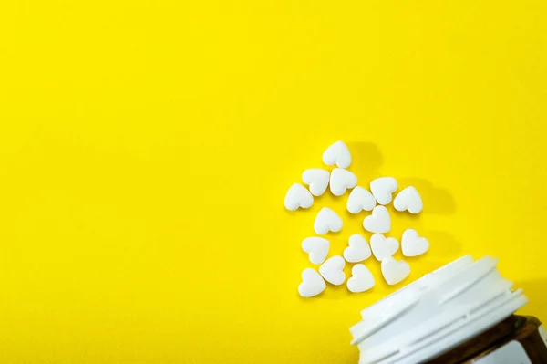 Pastillas blancas en forma de corazón sobre un fondo amarillo caen del frasco, productos farmacéuticos . — Foto de Stock