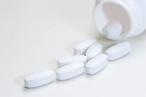 Las tabletas se vierten fuera del frasco sobre un fondo blanco. Vitaminas, medicamentos, vista frontal . — Foto de Stock