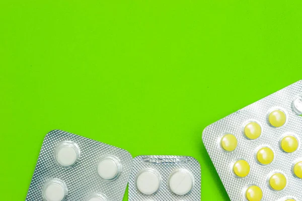 Tres paquetes brillantes de comprimidos blancos y amarillos sobre un fondo verde. Enfermedades, productos farmacéuticos . — Foto de Stock