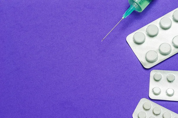 Tres paquetes brillantes de pastillas blancas y una jeringa médica con una aguja abierta sobre un fondo azul. Enfermedades, productos farmacéuticos . — Foto de Stock