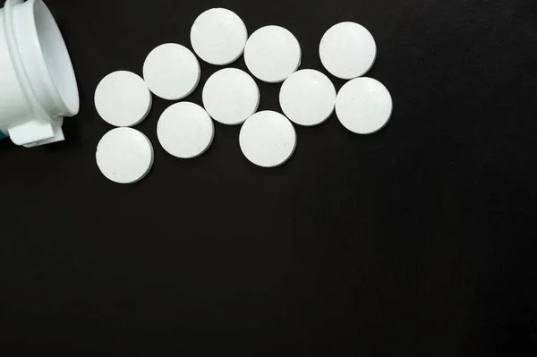 Las tabletas blancas salen del frasco sobre un fondo negro. Vitaminas, medicamentos, vista superior . — Foto de Stock