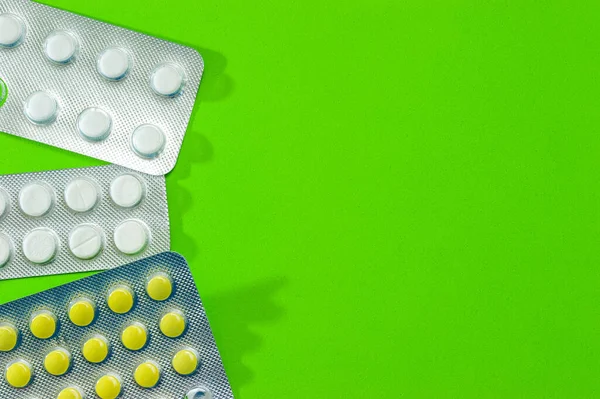 Tres paquetes brillantes de comprimidos blancos y amarillos sobre un fondo verde. Enfermedades, productos farmacéuticos . — Foto de Stock
