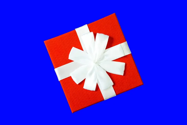 Una caja de regalo o regalo es de color rojo con un lazo blanco, en una vista superior de fondo azul. Estilo reclinado plano . — Foto de Stock