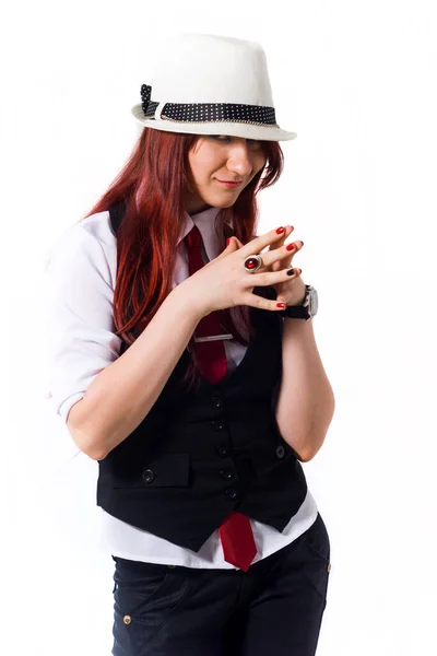 Una hermosa joven pelirroja con una blusa blanca, chaleco negro, corbata roja y sombrero blanco sobre un fondo blanco, mira hacia abajo desde debajo del borde de su sombrero . — Foto de Stock