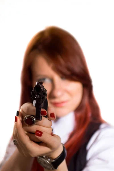 Rödhårig vacker flicka i vit skjorta, svart väst och röd slips, med en revolver i handen, siktar på betraktaren, på en vit bakgrund. — Stockfoto