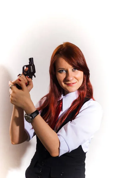 白いシャツ、黒いベストと赤いネクタイの赤い髪の美しい女の子は、彼女の手に銃を持ち、カメラを見て、白い背景に. — ストック写真