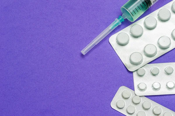 Tres paquetes brillantes de pastillas blancas y una jeringa médica con una aguja cerrada sobre un fondo azul. Enfermedades, productos farmacéuticos . — Foto de Stock