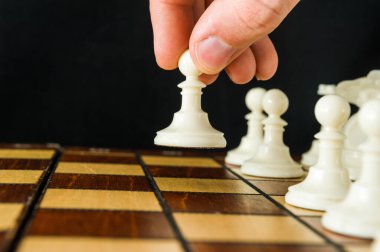 Bir satranç oyununda ilk hamleyi yapan adamın elinin bir piyonunu bir kare ileri taşıması. Koyu arkaplan.
