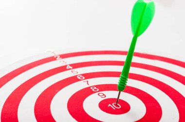 Hedefi vurmak için yeşil bir dartla tam isabet, başarı. Kırmızı ve beyaz daireli bir hedef..