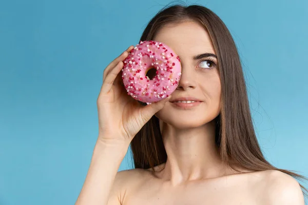 Крупним планом жінка з довгим волоссям тримає пончик. Жіноча модель пончик перед обличчям на синьому фоні . — стокове фото