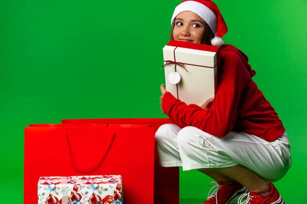 Sorrindo animado menina em vermelho santa claus roupa segurando presente de Natal em sua barba isolada no fundo verde — Fotografia de Stock