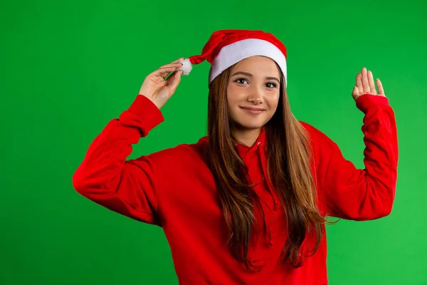 Jovem mulher em suéter vermelho e chapéu de Natal no fundo isolado verde — Fotografia de Stock