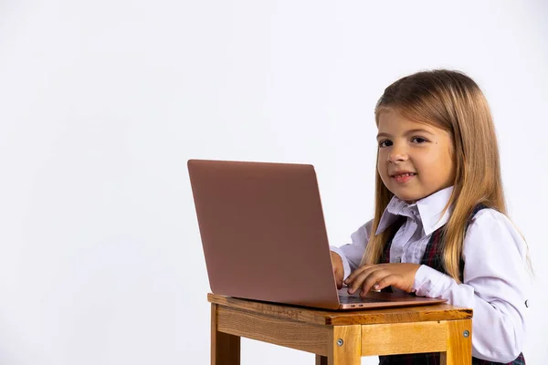 Chica joven sentada en la mesa en casa trabajando en su tarea de la escuela escribiendo una respuesta en un ordenador portátil —  Fotos de Stock