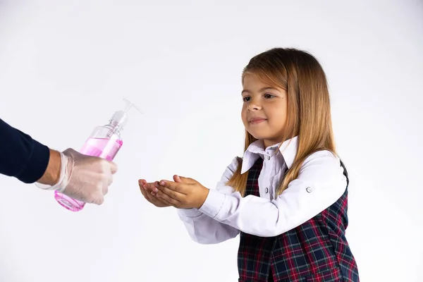 Маленька дівчинка з шкільною формою знезаражує руки гелем для дезінфекції алкоголю під час вірусу корони та спалаху грипу . — стокове фото