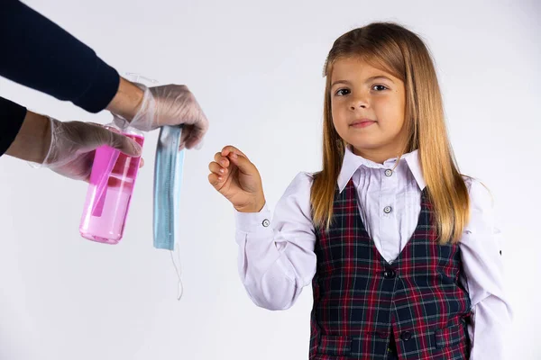 Caucásico chica con uniforme escolar toma máscara protectora y luego desinfectar sus manos, aislado sobre fondo blanco — Foto de Stock