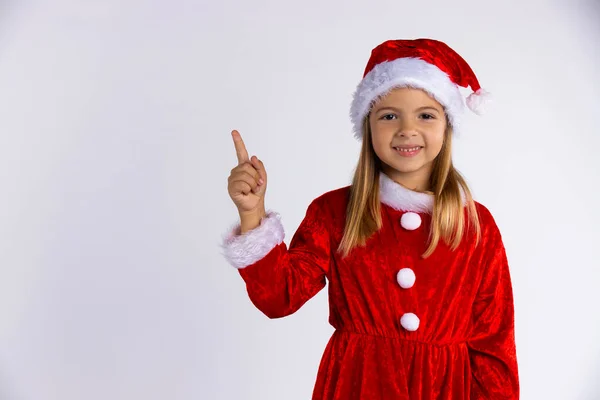 Niña en el sombrero de Santa y el traje con hermosa sonrisa señala el dedo. Aislado sobre fondo blanco — Foto de Stock