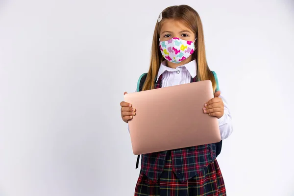 Özel maskeli bir kız, karantina ve tecritten sonra okula geri dönüyor. Okul formu ve dizüstü bilgisayar elinde.. — Stok fotoğraf